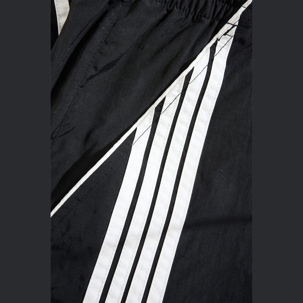 Detail of black water-resistant track pants featuring diagonal white stripes and elastic waistband for active wear.