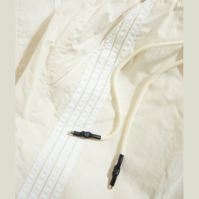 Cream men's track pants featuring elastic waistband, black drawstring aglets, and water-resistant polyester fabric.
