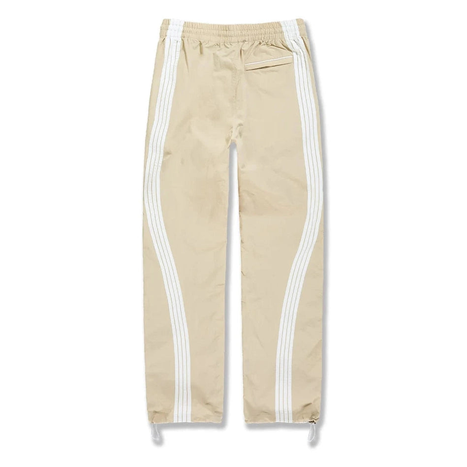 Beige water-resistant track pants with white side stripes, elastic waist, back pocket, and drawstring cuffs for active wear.