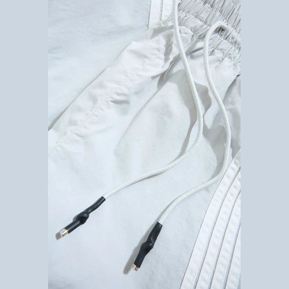White track pant waistband featuring elastic gather, white drawstrings with black aglets, and side stripe detailing.